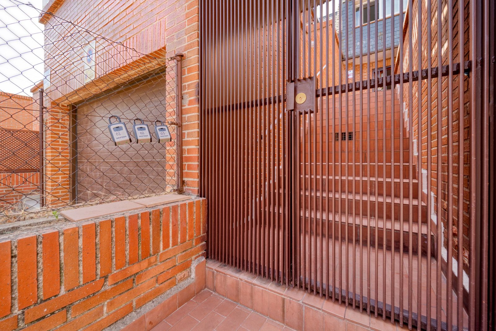 Locked metal security gate across a brick areaway with steps leading to a lower apartment entrance