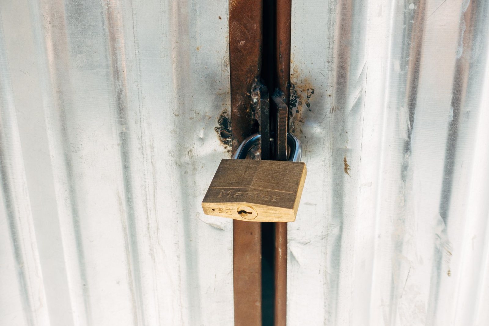 Brass padlock on a welded hasp securing a corrugated metal gate