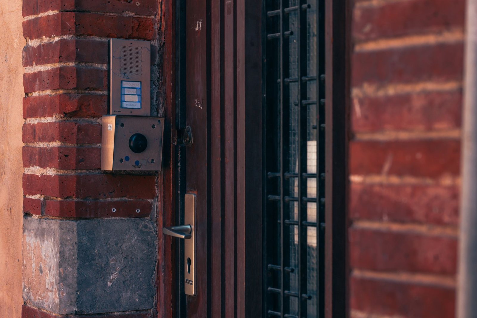 Apartment building entrance door with a lever handle, keyed cylinder and an intercom panel on the brick beside it