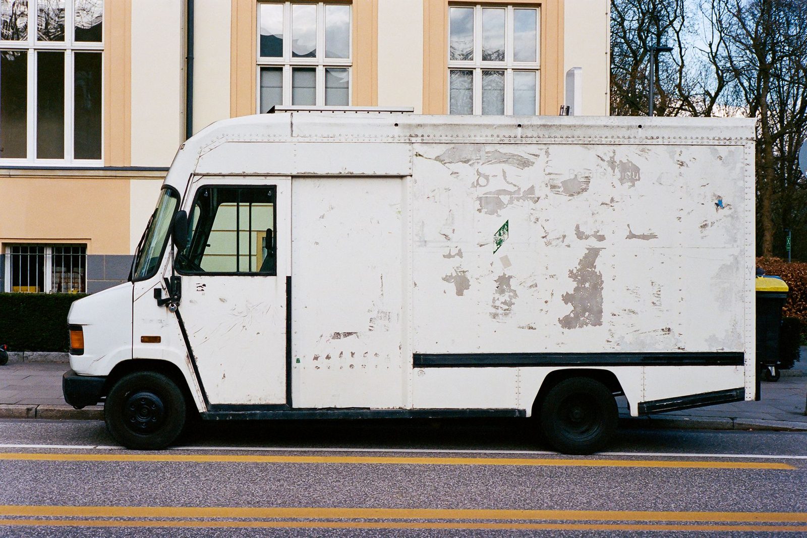 White work van parked at the curb on a city street beside an apartment building