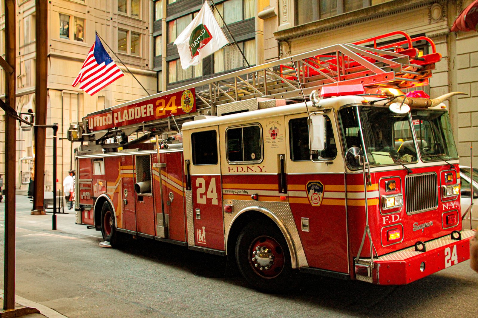 FDNY Ladder 24 fire truck parked on a narrow Manhattan street beside a stone building facade