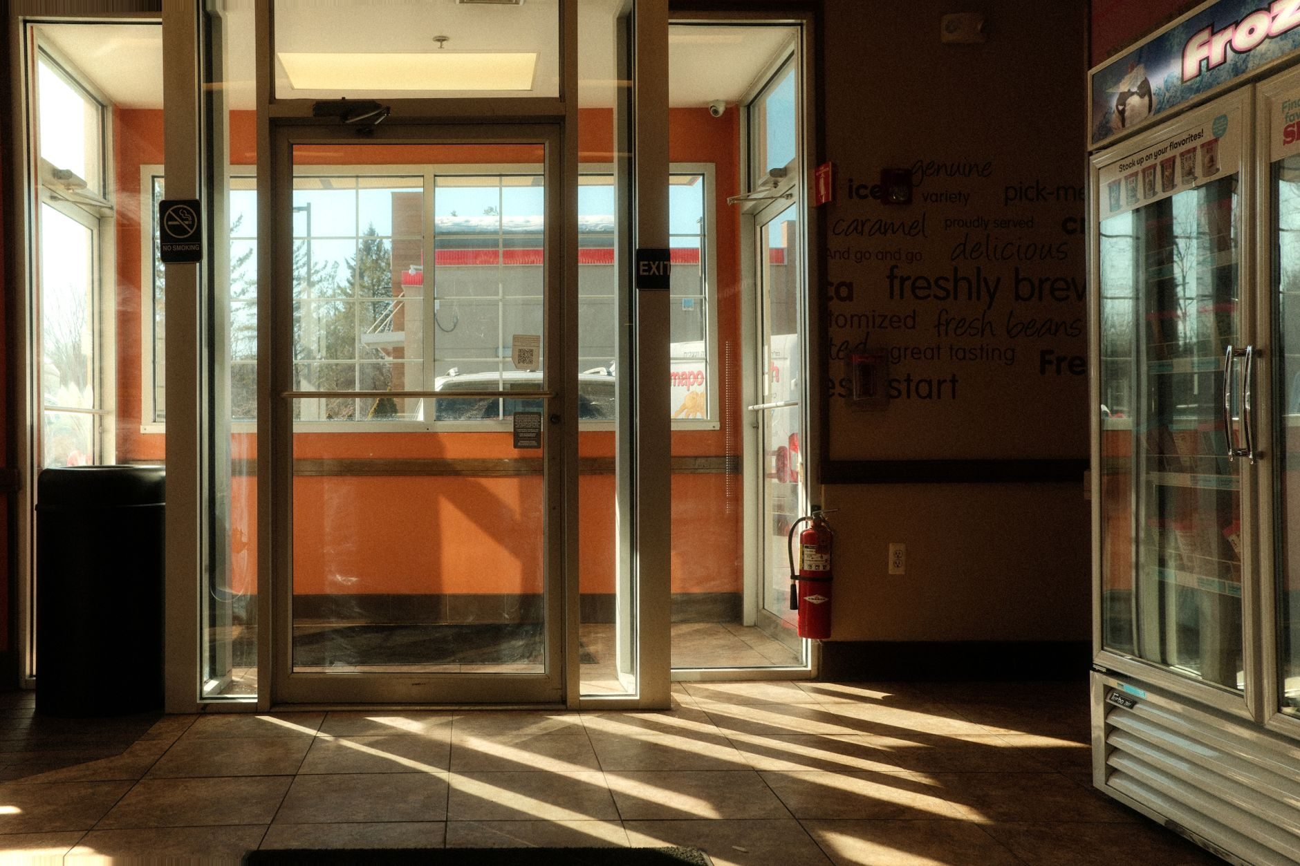 Aluminum-framed glass storefront entry doors seen from inside a shop, with an overhead door closer, push-pull hardware and an exit sign above the vestibule