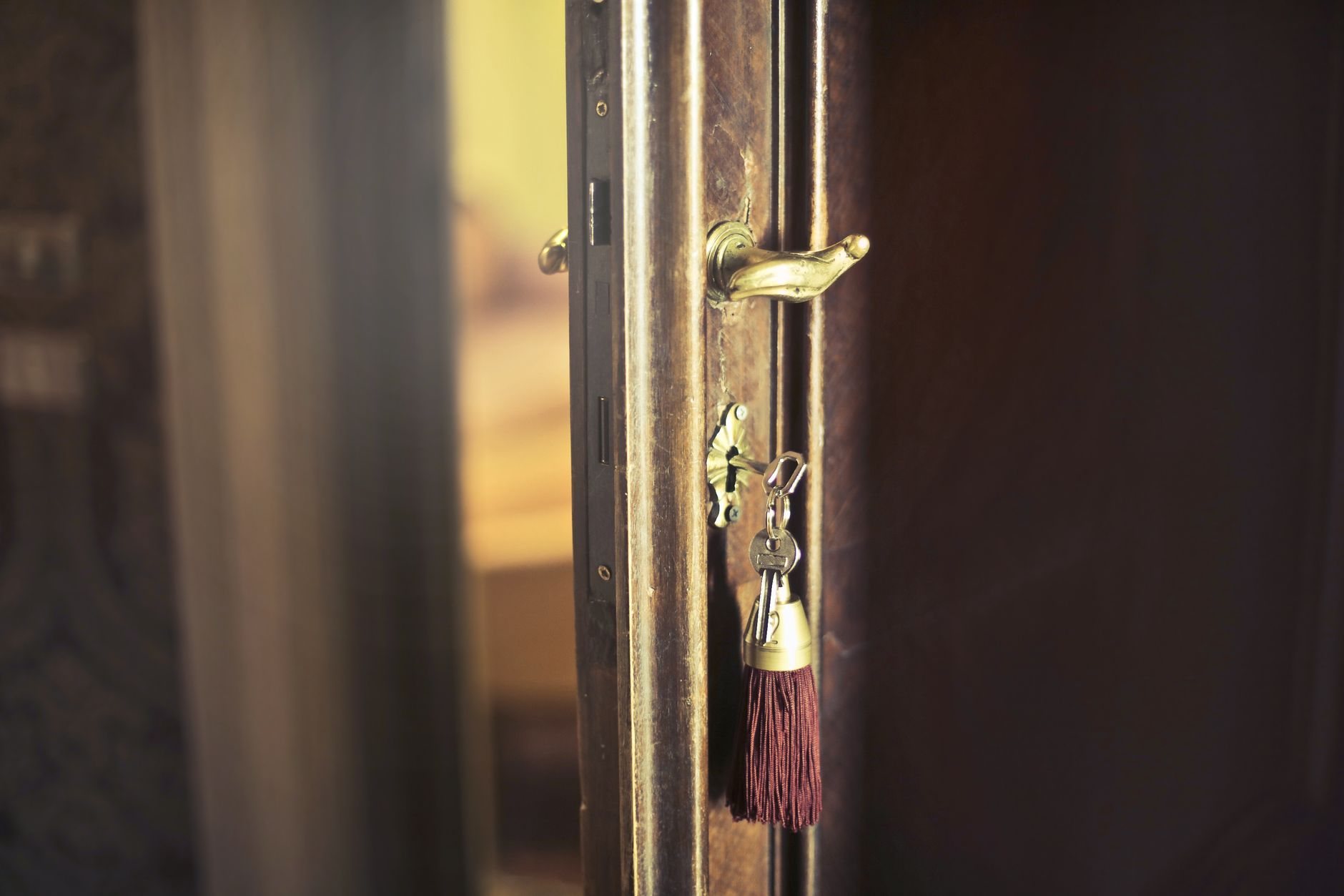 A set of keys left hanging in the keyhole of a wooden apartment door fitted with a brass lever handle and mortise lock