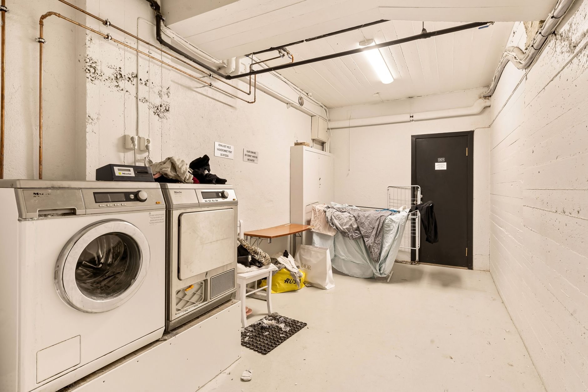 Shared basement laundry room in an apartment building with washers, dryers and a steel entry door