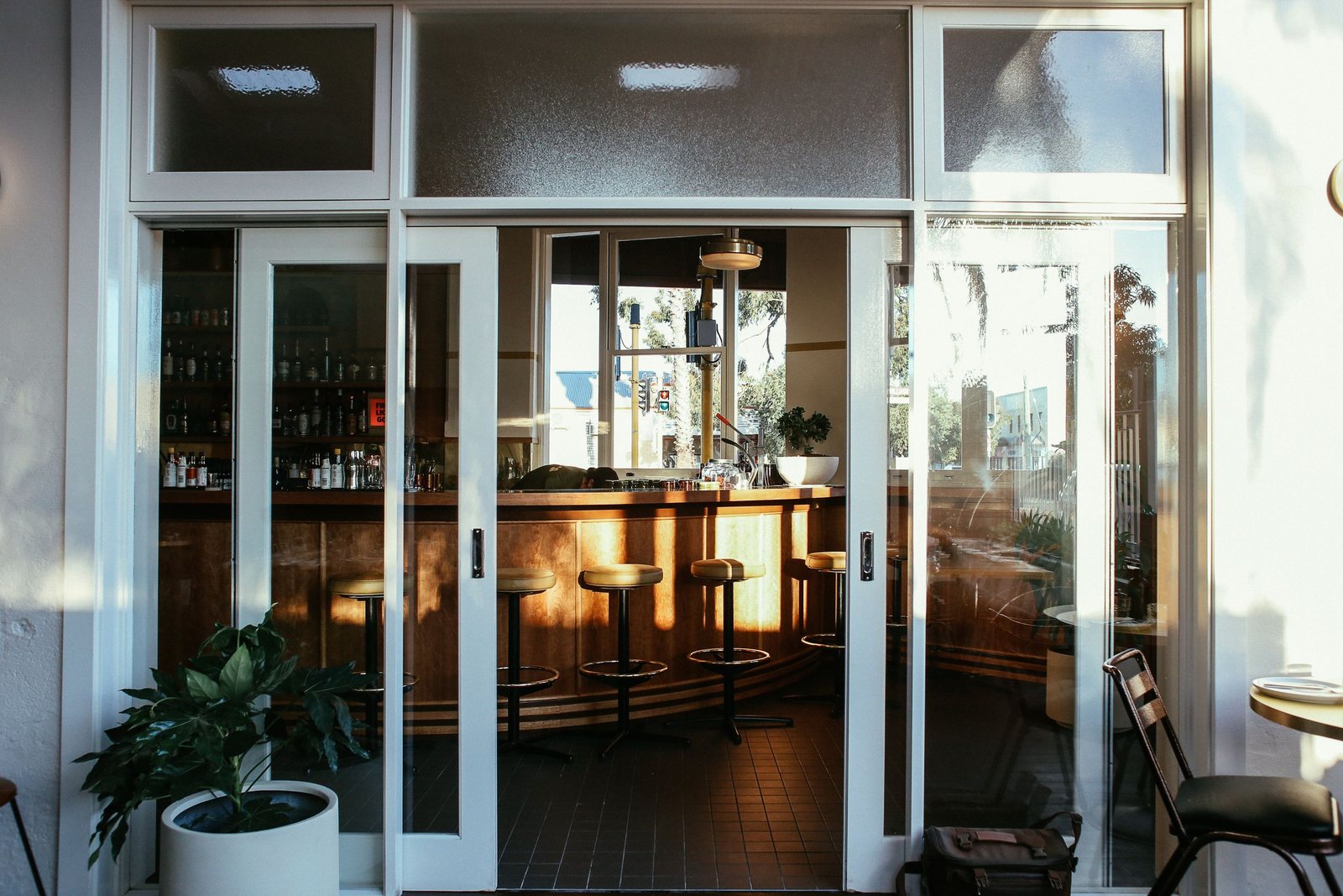 Glass entrance doors of a bar open onto a wooden counter and row of stools inside