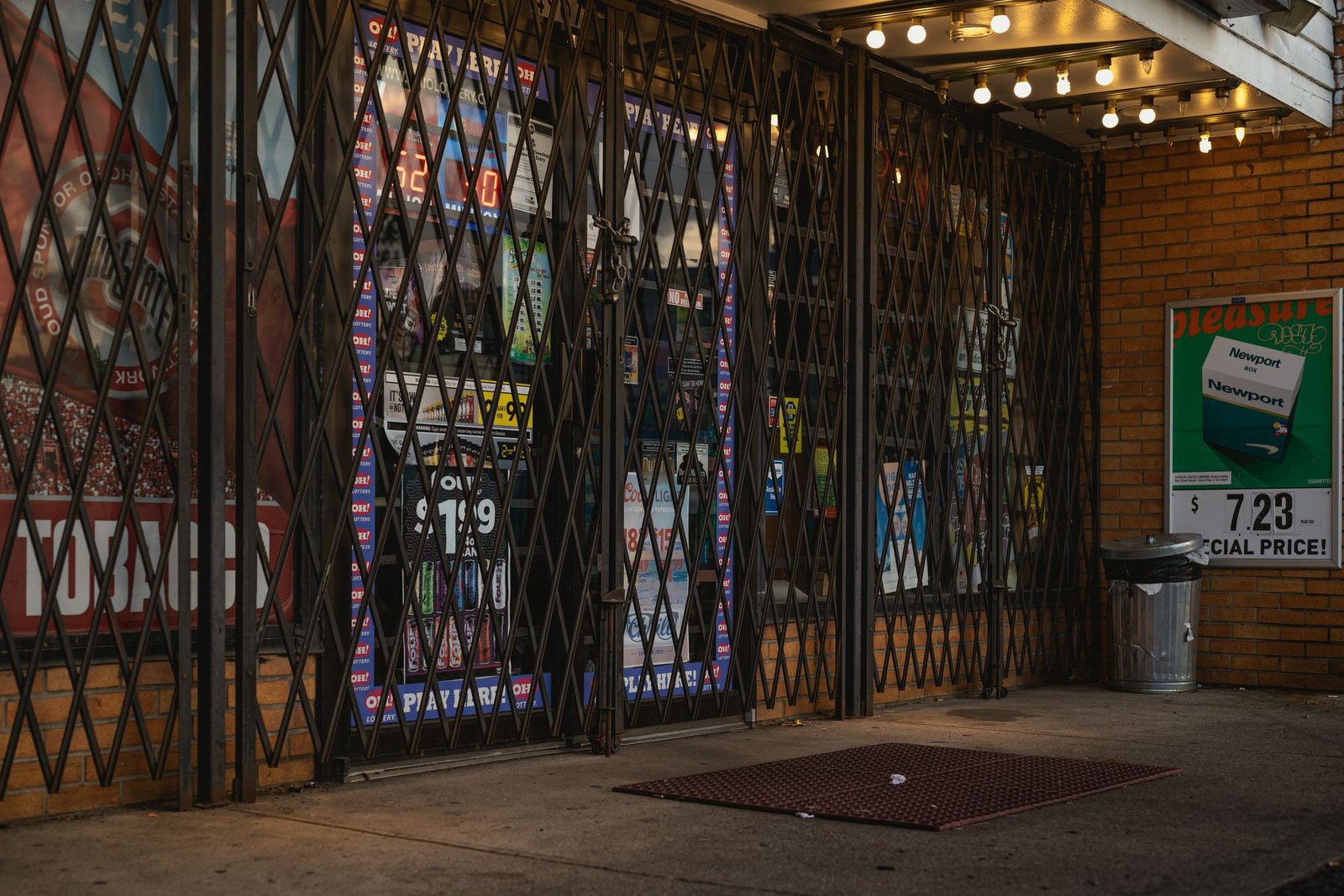 Closed steel accordion security gate pulled across the front of a New York City corner store at dusk