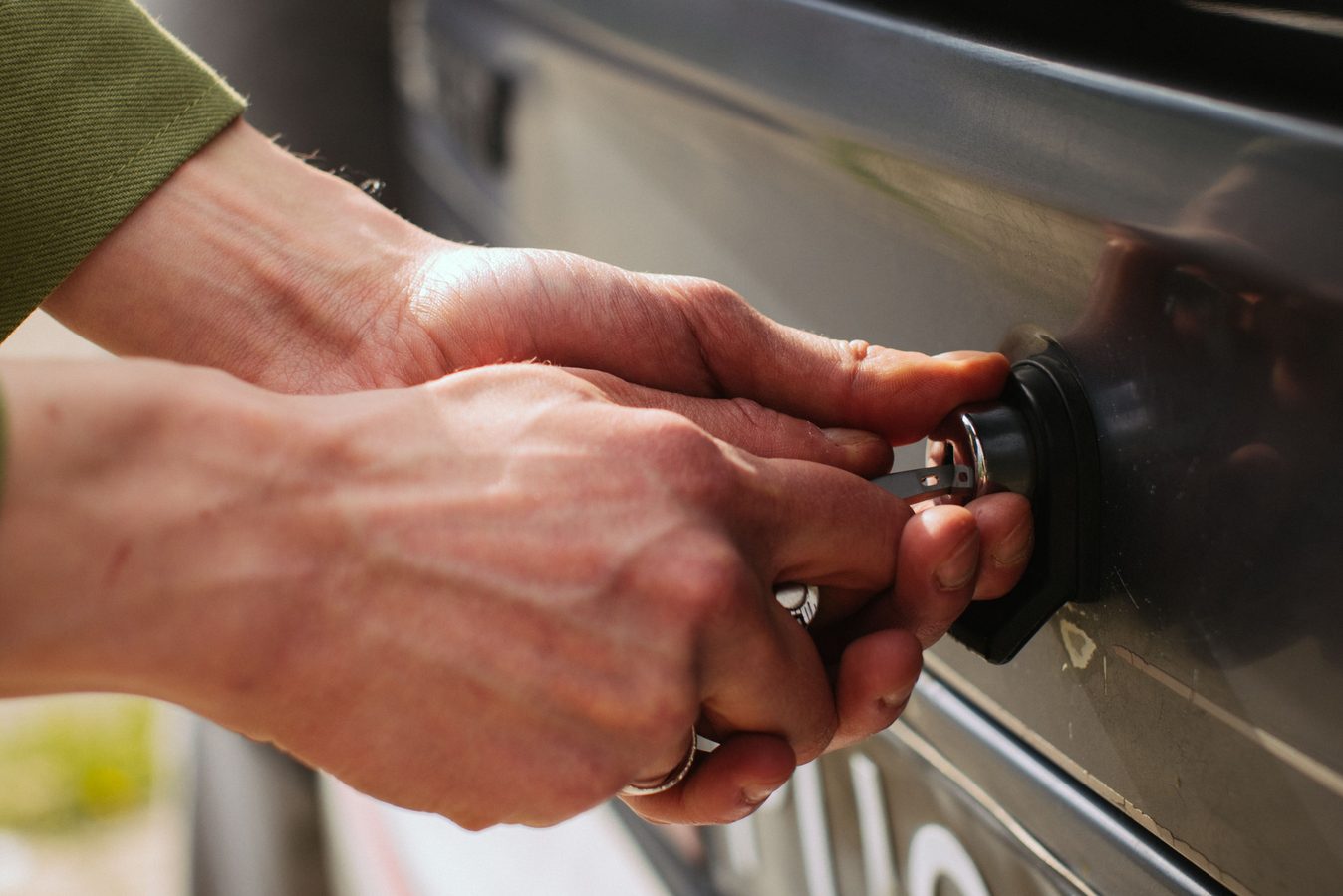 Hands turning a key in the rear lock of a car to open the trunk