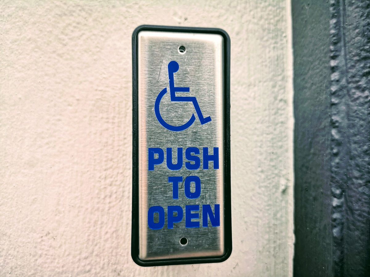 Accessibility push button sign mounted on a wall beside an entrance