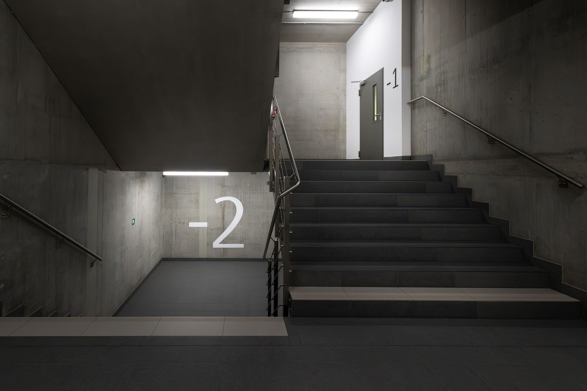 Concrete building stairwell with marked lower levels and a fire-rated access door at the landing