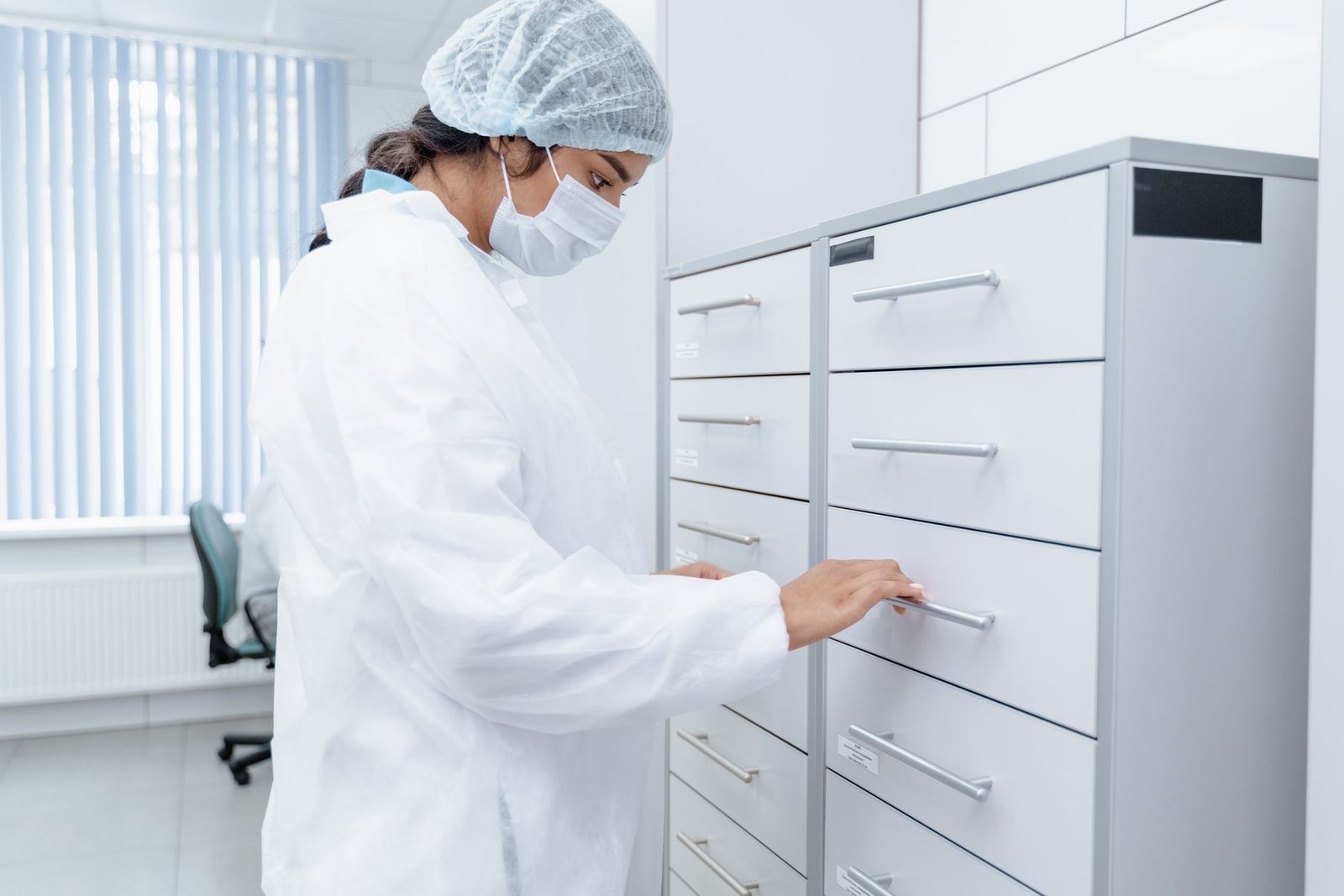 Clinic staff member in a white coat opening a drawer in a row of metal records and supply cabinets
