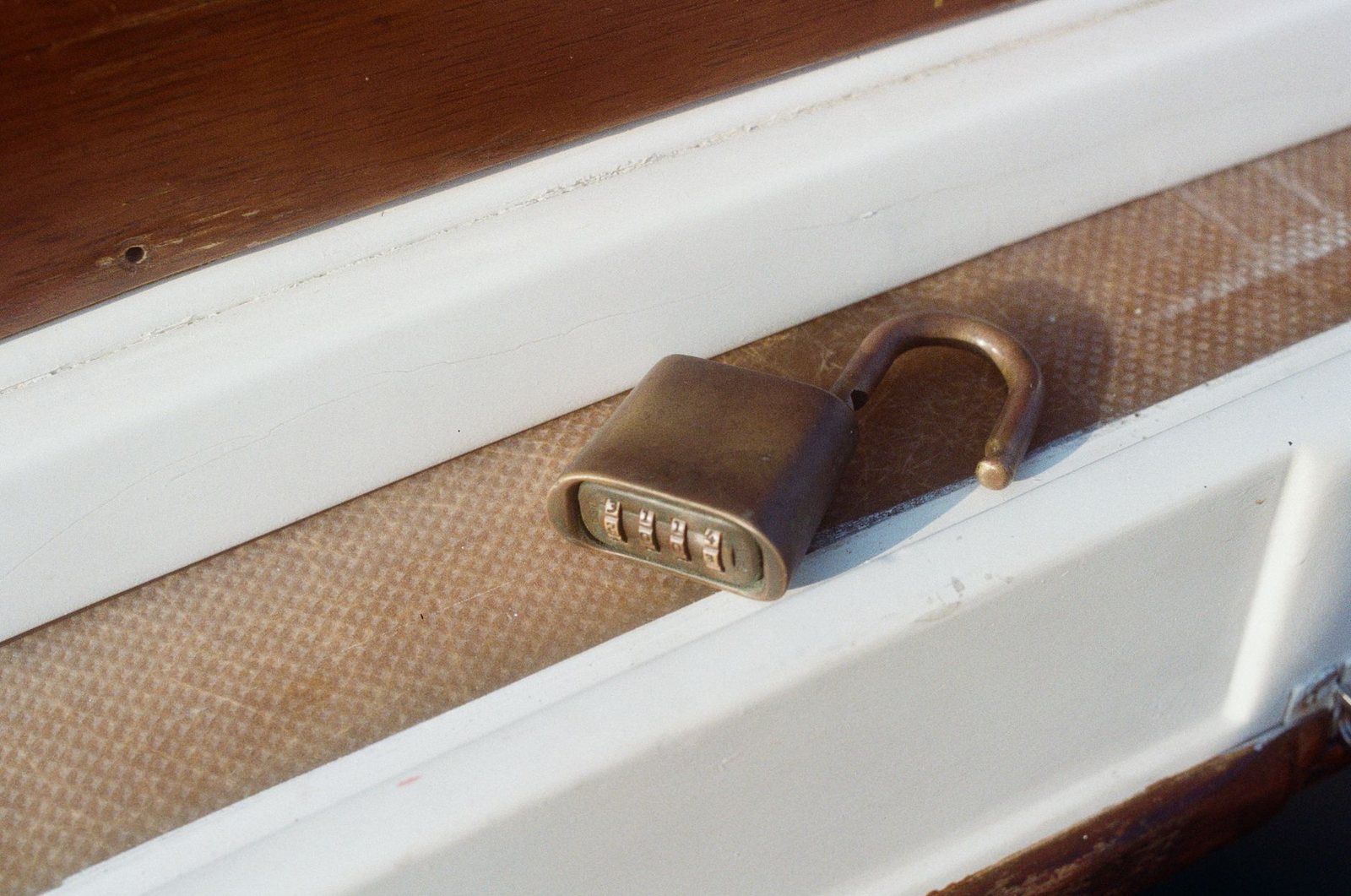 Worn four-dial combination padlock sitting open on a painted sill
