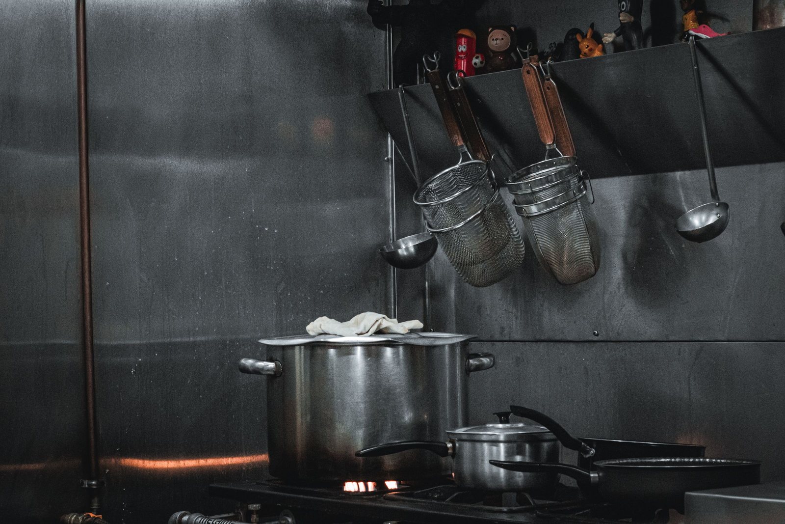 Stainless steel commercial kitchen line with a stockpot on the range and utensils hanging above