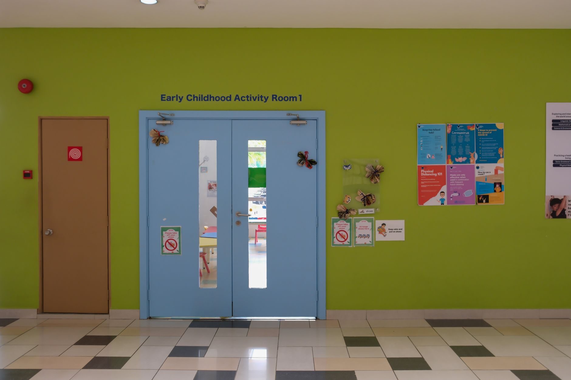Entrance to a childcare activity room with a pair of doors fitted with surface door closers, narrow vision panels and a lever handle