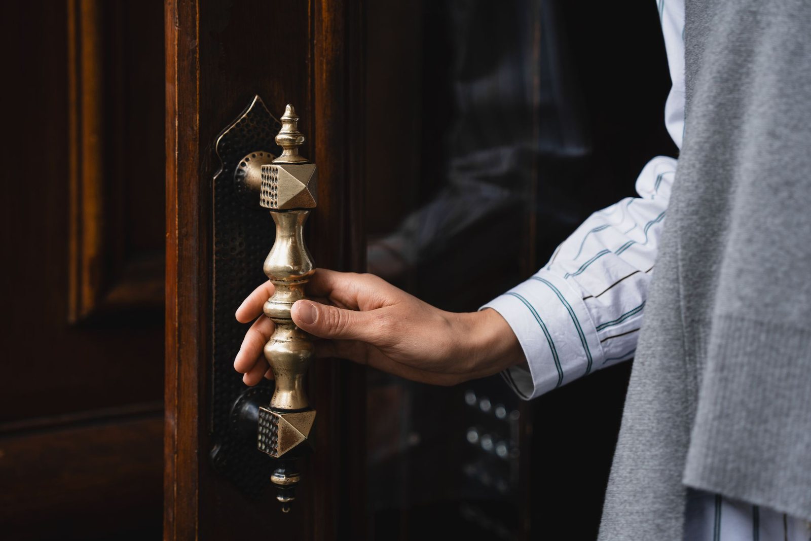 Hand resting on the brass handle of an old wooden entrance door while checking that the latch and hardware operate smoothly