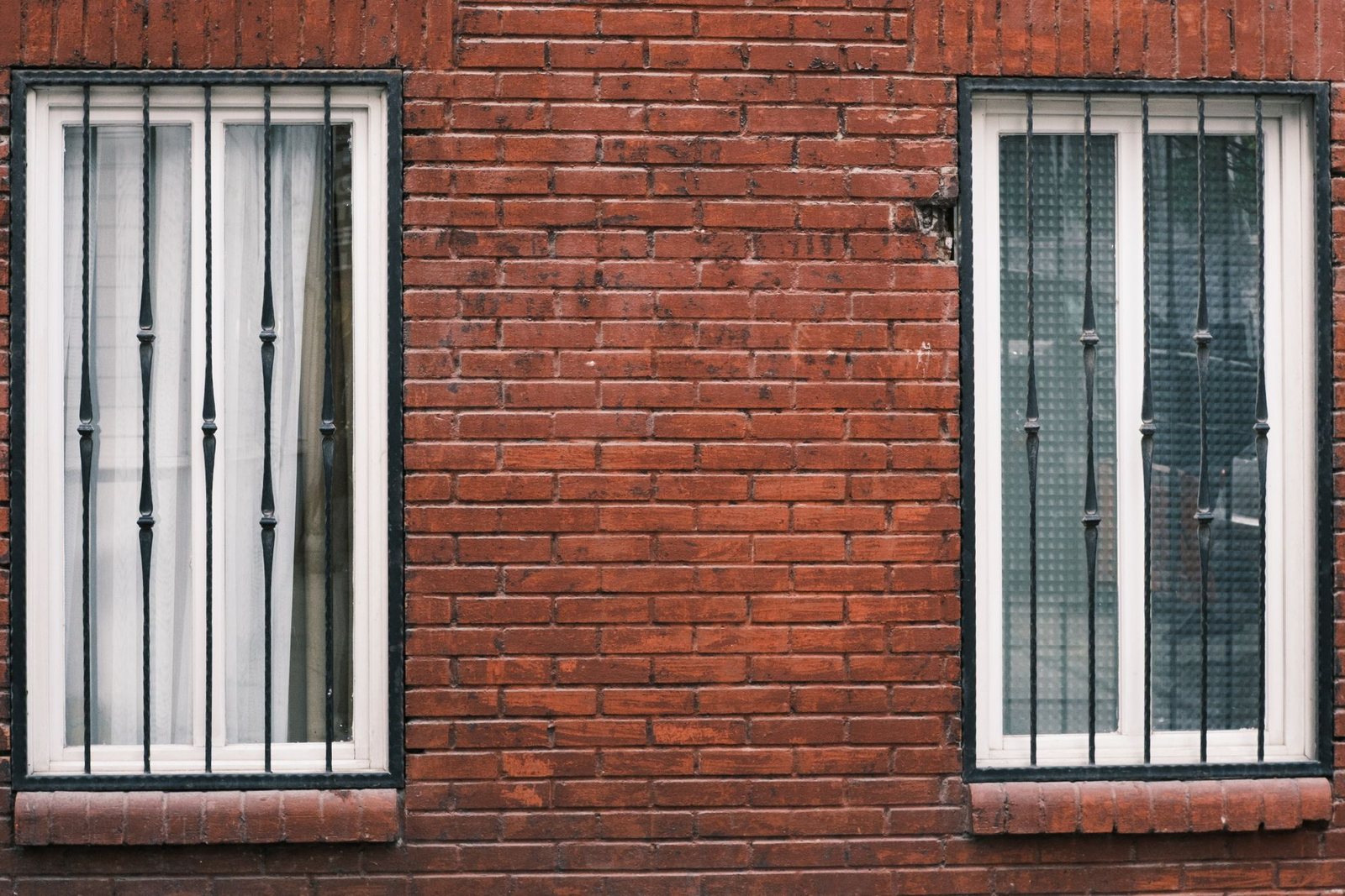 Two ground-floor windows fitted with ornamental iron security bars on a red brick New York building