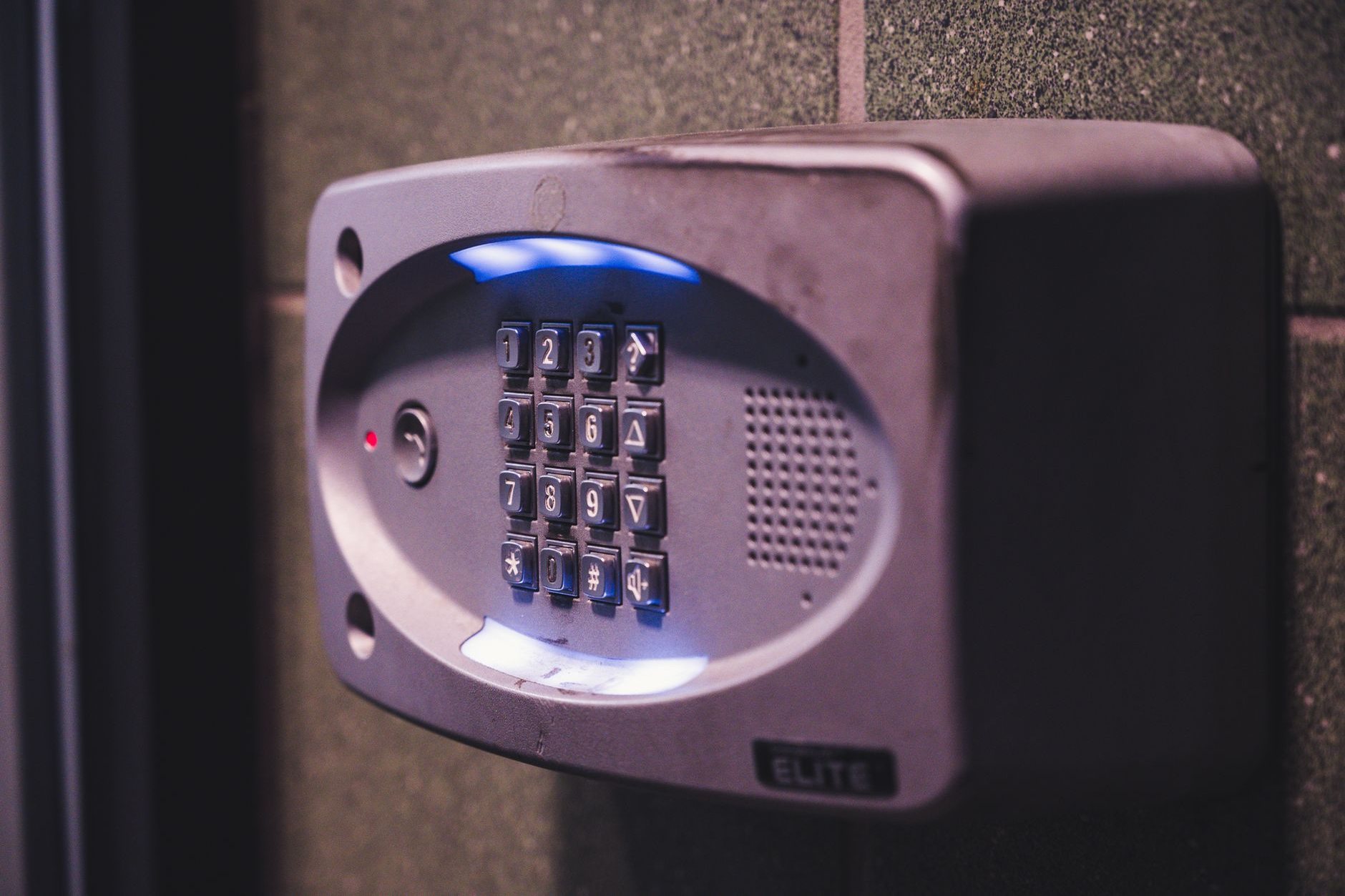 An illuminated keypad entry panel with a call button mounted beside a building entrance door