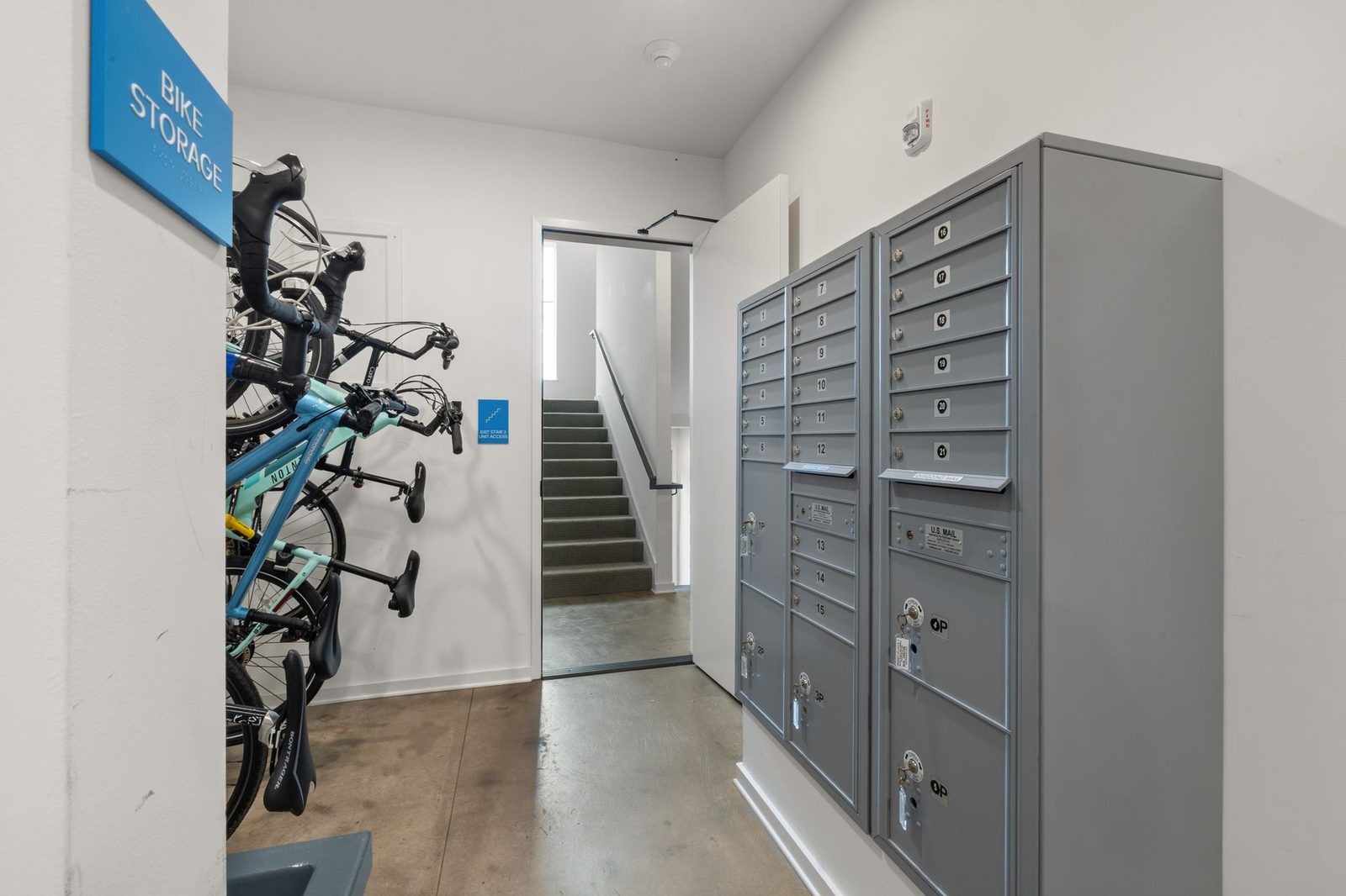 Building mailroom with a bank of numbered metal mailboxes and parcel compartments beside a bike storage area and stairwell