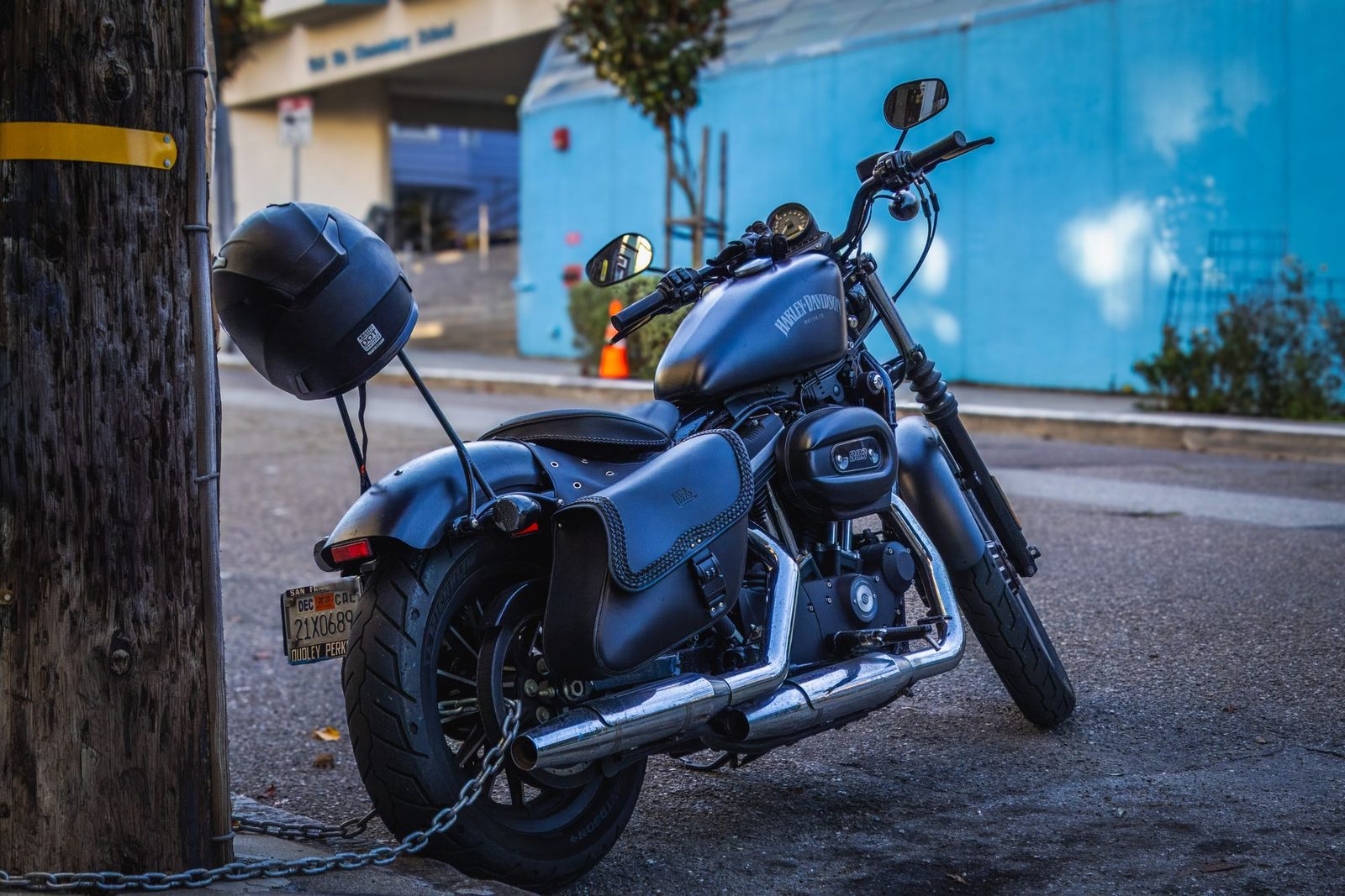 Motorcycle parked at the curb on a city street and chained to a utility pole with a helmet secured to the frame