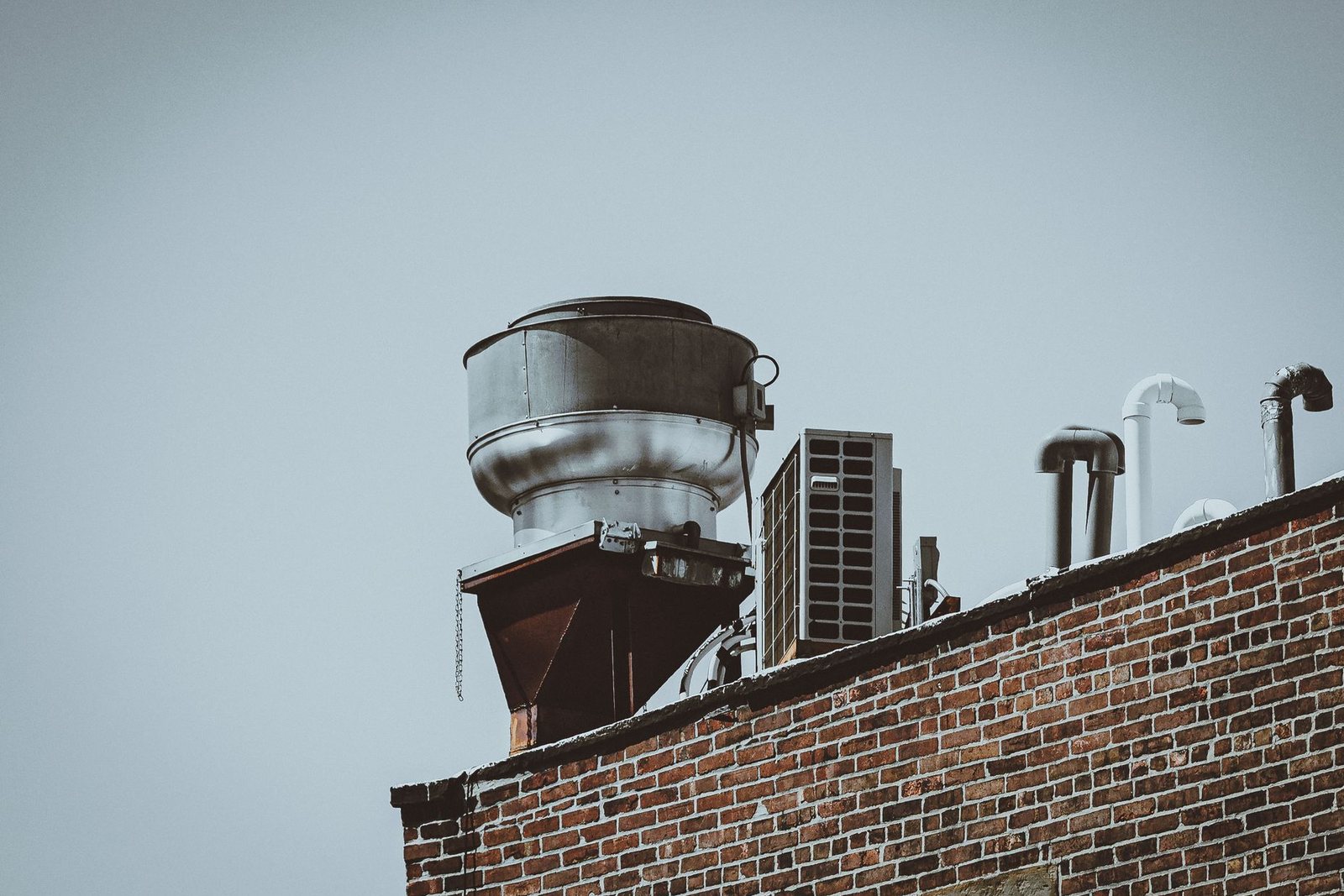 Rooftop exhaust fan, condenser unit and vent pipes above the brick parapet wall of a New York City building