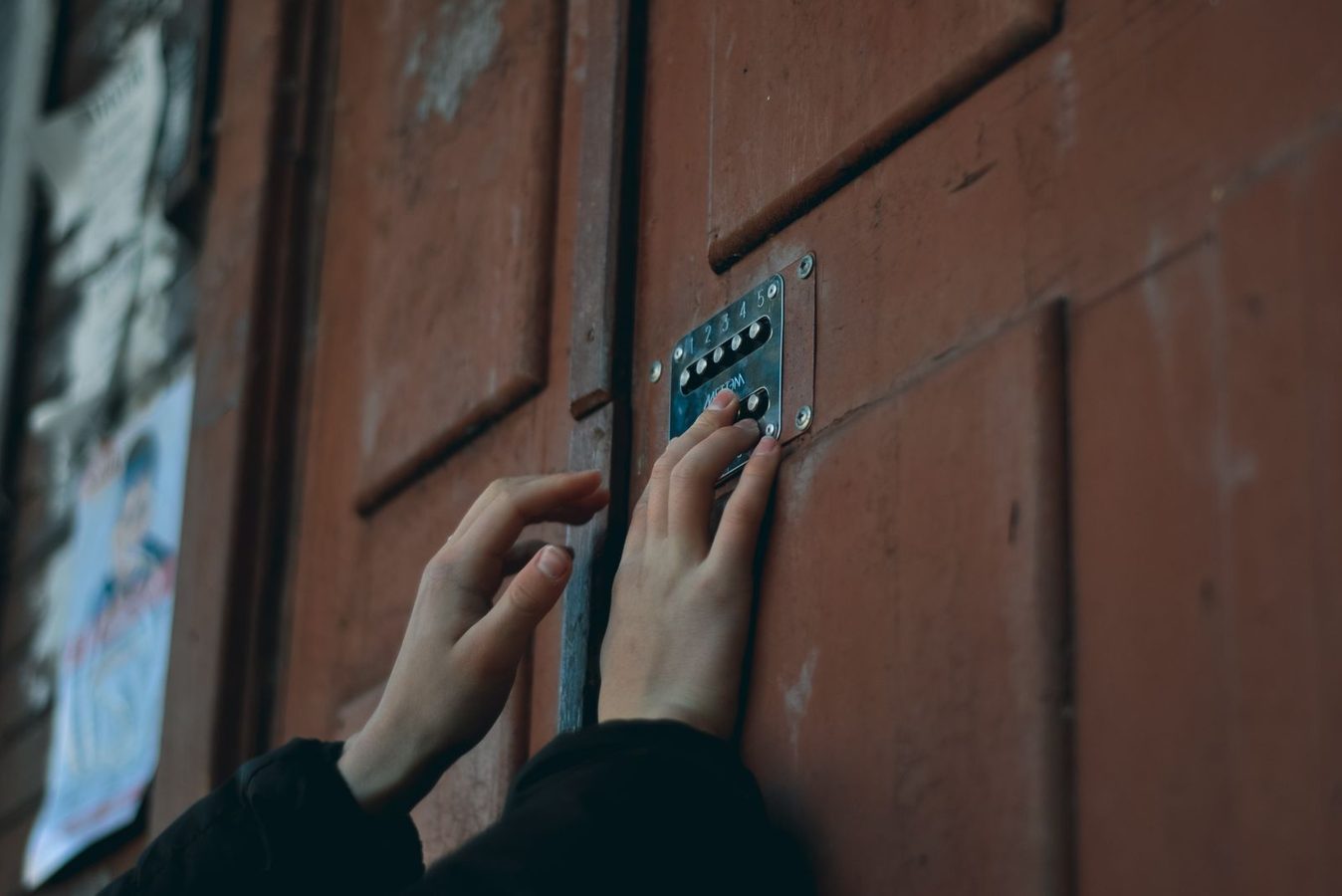 Hand entering a code on a pushbutton keypad lock mounted on a building entrance door